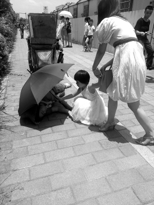 路过的小女孩用伞为女清洁工挡太阳。《新快报》昨日刊图
